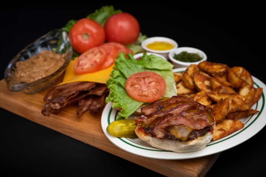 A burger with bacon, lettuce, tomato, Cheddar, mayo, mustard, relish, ketchup and crunchy peanut butter with a side of fries.